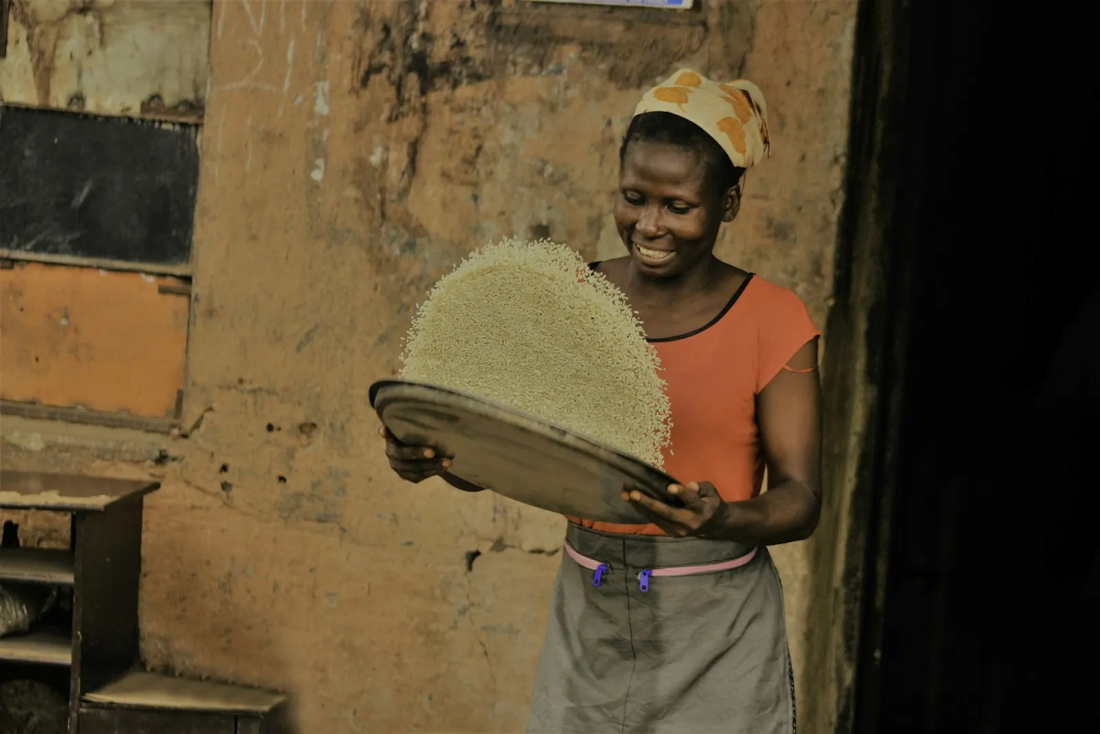 A woman in Lagos winnows Ofada rice on a round tray outside her shop
