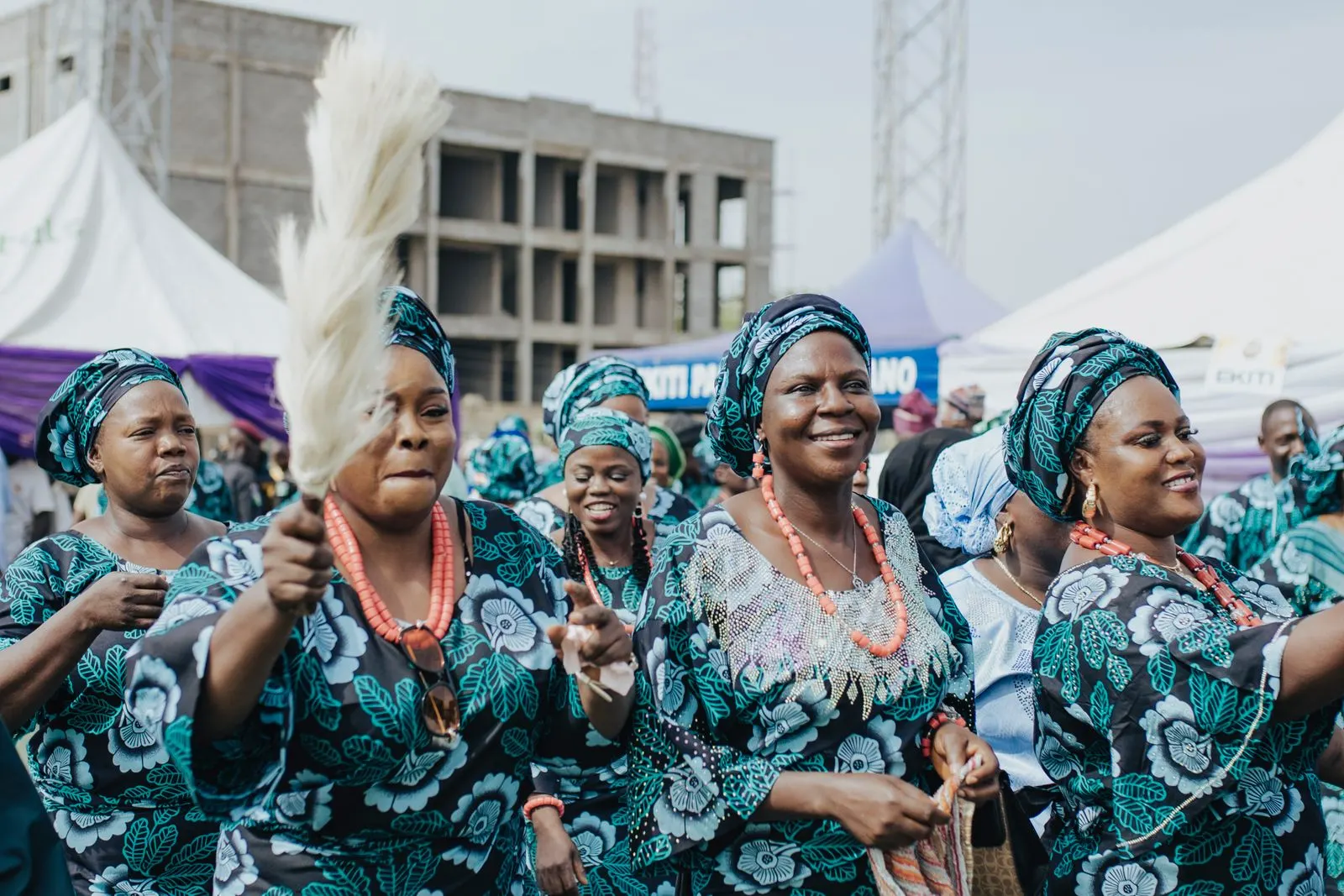 A crowd of women in matching aso ebi dance together at an outdoor celebration