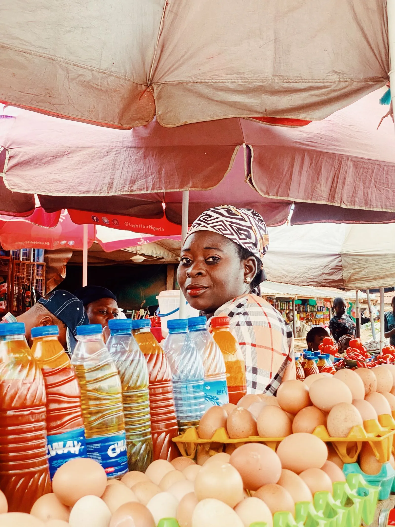 A trader in Ife sells eggs and cooking oil from her stall under market umbrellas