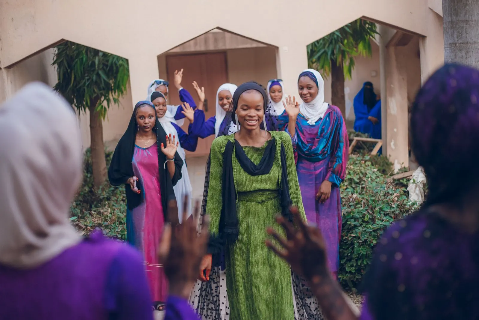 A group of young women in colourful dresses wave and celebrate together outdoors