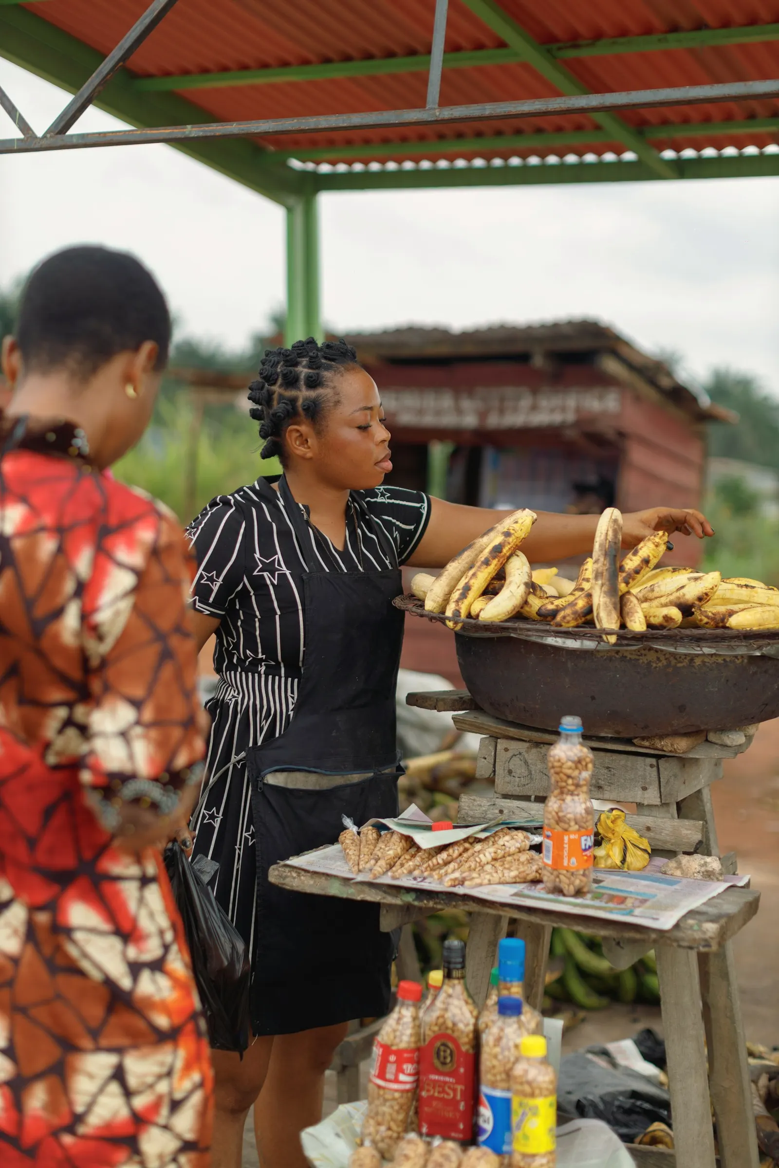 A trader in Benin City lays out roasted plantain for a customer at her roadside stall