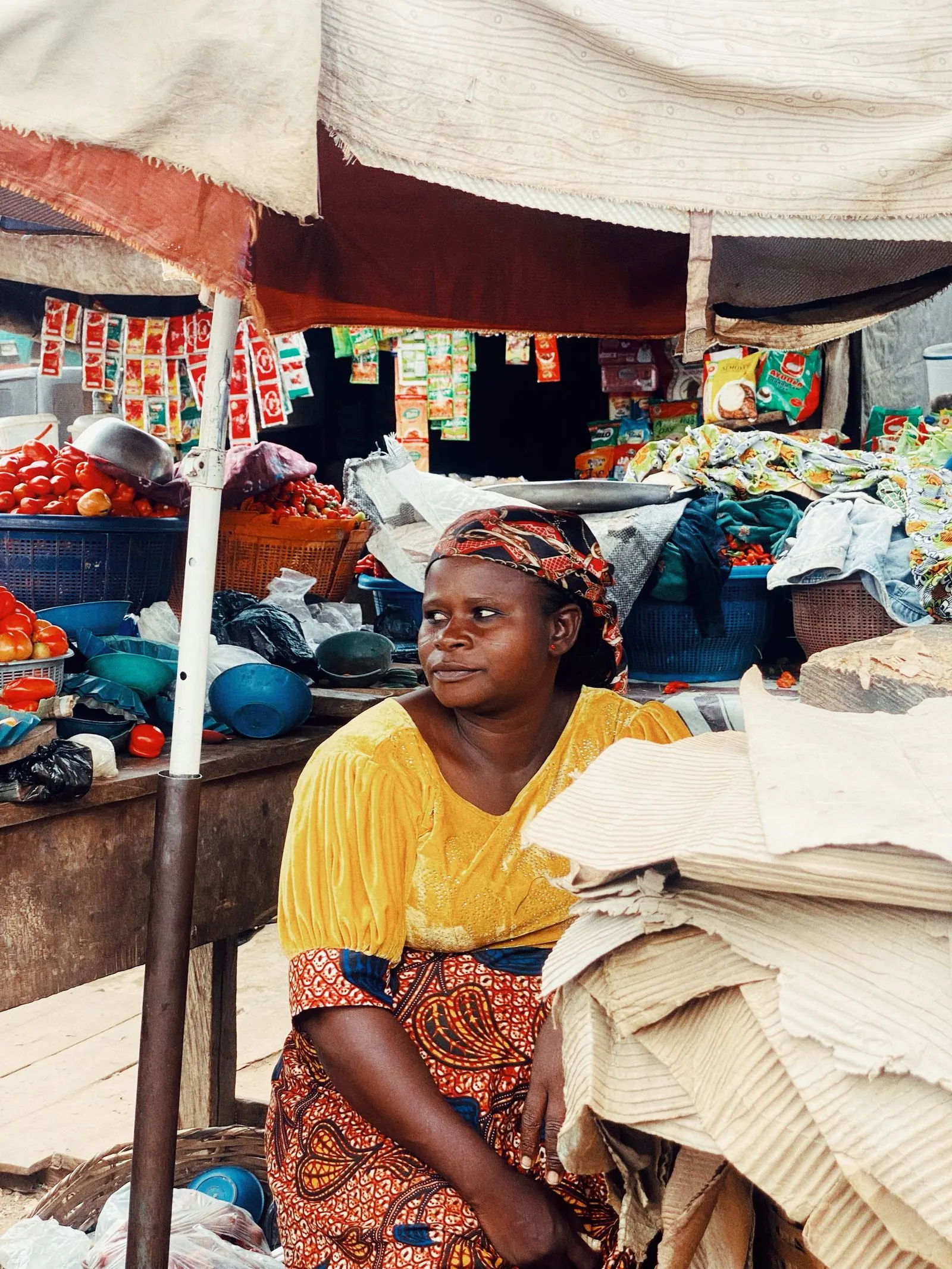 A trader in Ife sits at her market stall among fabric and produce